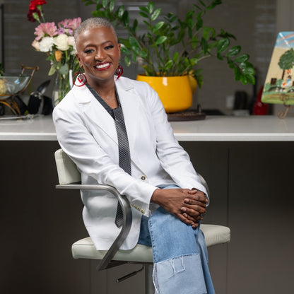 Woman sitting on a chair in a kitchen setting with flowers and plants in the background.